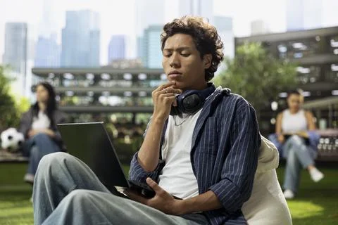 Focused student thinking while using laptop on outdoor campus lawn Stock Photos
