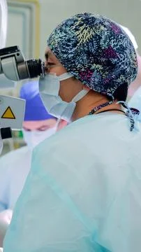 Focused surgeon wearing patterned cap, mask, protective eyewear, and sterile Stock Photos