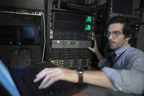Focused technician with laptop working at server panel in server room Foto stock