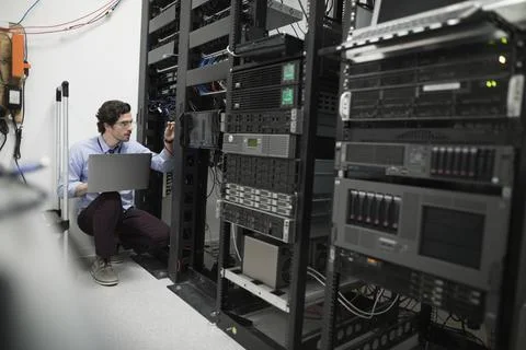 Focused technician with laptop working at server panel in server room Foto stock
