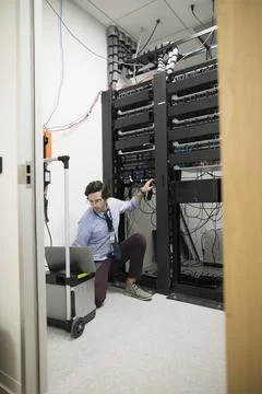 Focused technician with laptop working at server panel in server room Foto stock