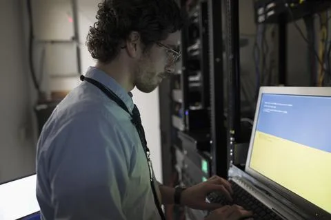Focused technician with laptop working at server panel in dark server room Foto stock