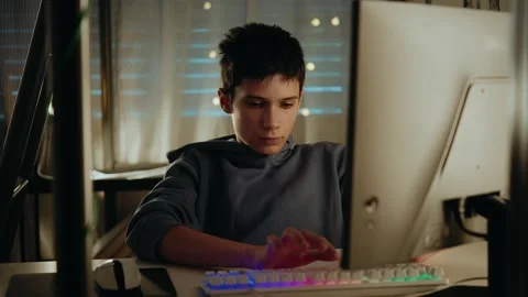 Focused Teenage Boy Typing on a Computer with a Colorful Keyboard at Night Stock Footage 336316969