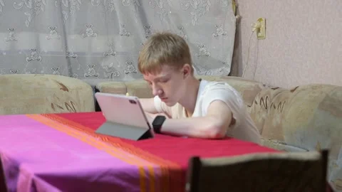 Focused Teenage Boy Using Tablet Computer at Home Table Stock Footage 329097812