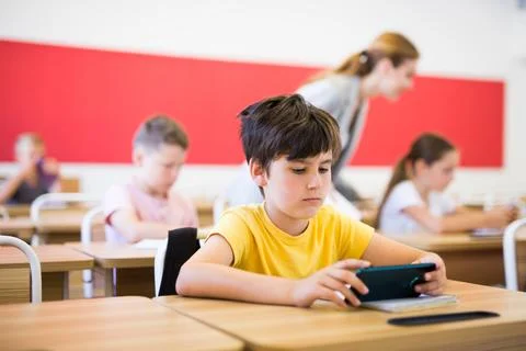 Focused tween schoolboy using mobile phone at lesson in class Stock Photos