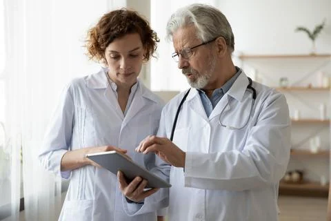 Focused two different generations doctors using computer tablet. Stock Photos