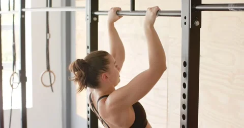 Focused unaltered caucasian woman training at gym doing pull ups on bars, in Stock Footage 337096458