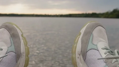 Focused view of white sneakers at foreground and defocused view of river at Stock Footage 143595566