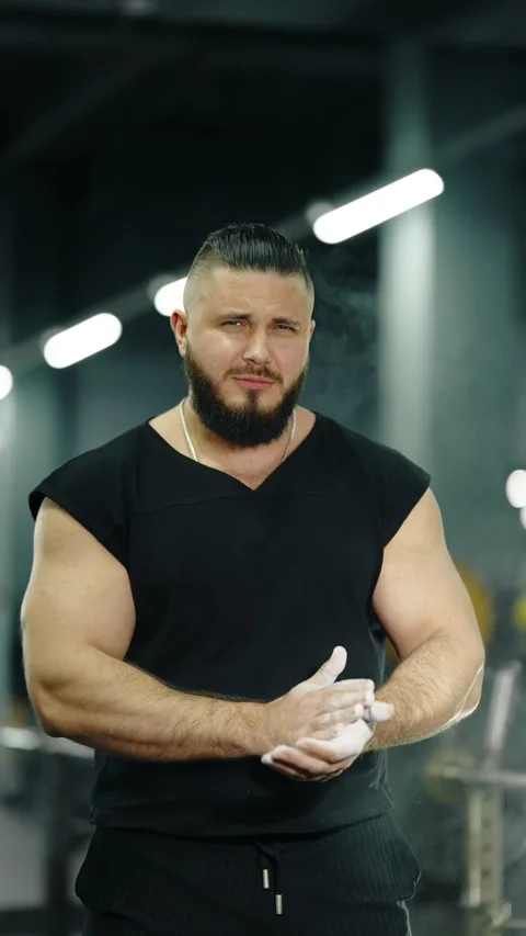 Focused weightlifter claps chalk and faces the camera in a dimly lit gym 库存影片 329555740
