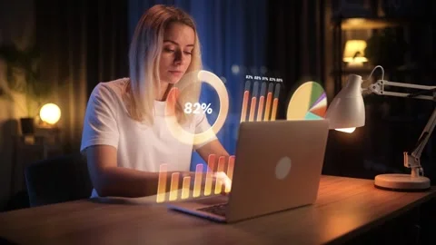 Focused woman analyzing data on laptop with futuristic holographic charts at Stock Footage 303287008
