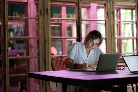 Focused woman freelancer working on computer in cafe, female taking notes while Stock Photos