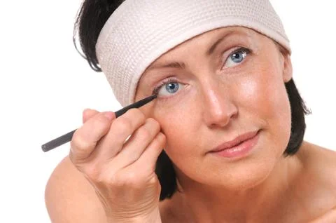 Focused woman looking at camera while putting eyeliner Stock Photos