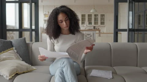 Focused Woman Reading Documents On Couch In Bright, Modern Living Room Stockbeeldmateriaal 306698110