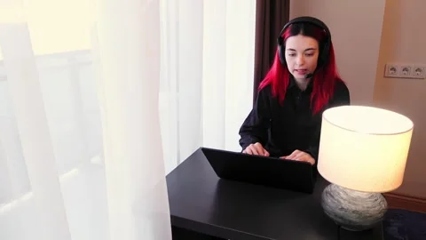 Focused woman is using computer wearing headset and talking during video call Stock Footage 343950736