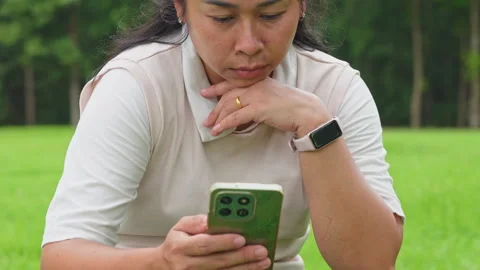 Focused woman using mobile phone checking screen while sitting outdoors in park Stock-Footage 343486520