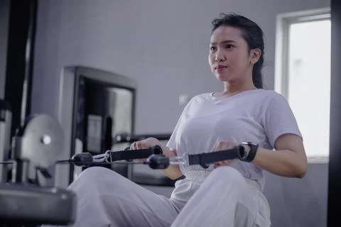 Focused woman using rowing machine for strength training session Stock Photos