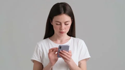 A focused woman wearing basic T-shirt is using her smartphone  Stock Footage 154947428