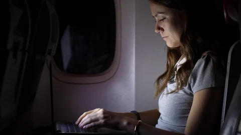Focused woman work on computer in airliner at night Stock Footage 98737973