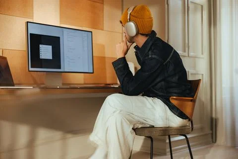 Focused work happens at a computer desk with headphones in a home office Stock Photos