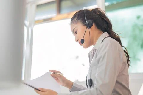 Focused Work. Woman taking notes while on a headset in a modern office setting. Foto stock