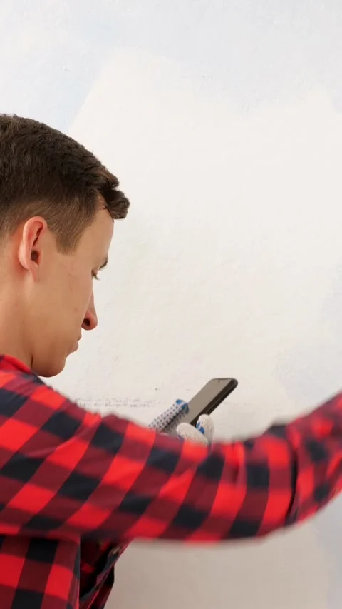 Focused worker checking his smartphone while painting a wall white, multitasking Stock Footage 341677099
