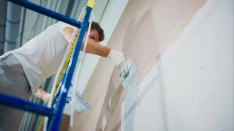 Focused Worker on a Ladder Applying Paint to a Wall in an Indoor Environment Stock-Footage 316056964