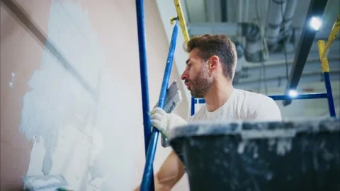 A Focused Worker Skillfully Applies Drywall Compound on a Wall While Balancing Vídeo Stock 316057897