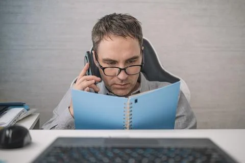 Focused worker talking on smartphone while reviewing notes in office, managin Stock Photos
