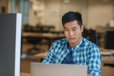 Focused young Asian designer using a laptop at his desk Stock Photos