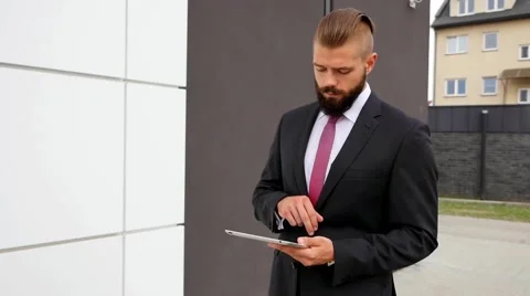 Focused young bearded businessman using his tablet pc. Outdoor photo. Stock Footage 60944839