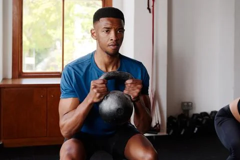 Focused young black man doing kettlebell squats at the gym Stock Photos