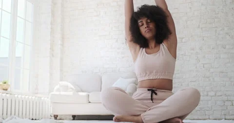 Focused young black woamn sits mat, legs crossed, doing yoga breathing exercise. Video stock 157978902