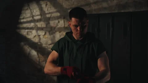 Focused young boxer wrapping hands with red bandages in locker room 库存影片 337248675