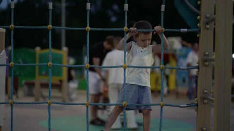 Focused young boy climbs blue rope net at outdoor playground, showing determinat Video stock 341410033