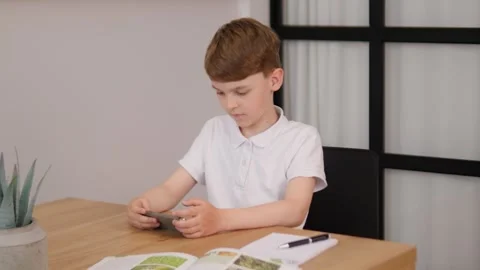 A focused young boy is deeply engaged with his mobile device while at home Stock Footage 312196156