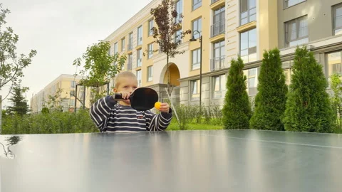A focused young boy holds a black ping pong paddle and a yellow ball Stock Footage 344972163