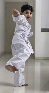 Focused young boy performs a high kick in karate uniform, showcasing energy Foto stock