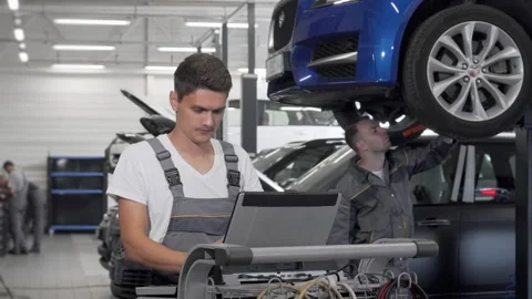 Focused young car mechanic using laptop for diagnostics in a busy garage Stock Footage 311939798