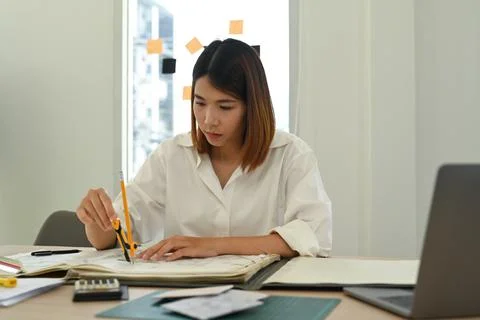 Focused young female architect using laptop and working on blueprint at her Stock Photos