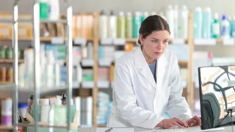 Focused young female pharmacy worker in white coat using desktop computer to Stock Footage 331315007