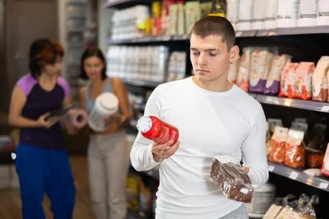 Focused young guy choosing high-protein bread and supplement in sports nutrition Stock Photos