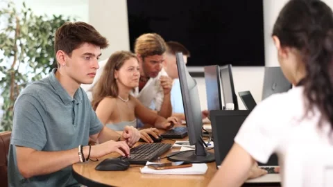 Focused young guy studying in computer lab with fellow students engrossed in Stock Footage 304707816