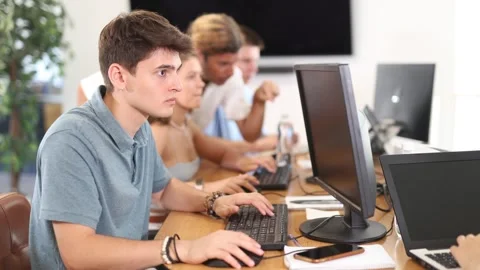 Focused young guy studying in computer lab with fellow students engrossed in Stock Footage 310067447