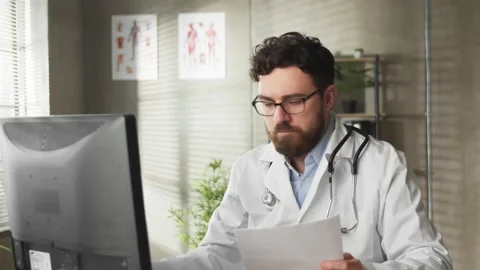 Focused young male general practitioner in glasses wearing white uniform Stock Footage 169015593