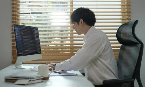 Focused young male programmer working on computer software, sitting at desk.. Stock Photos