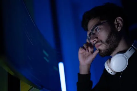 Focused young man analyzing data on a computer screen in a dimly lit room d.. 库存照片
