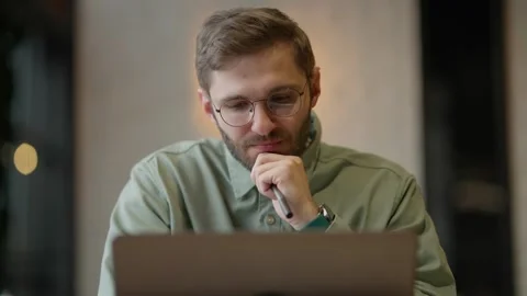 Focused Young Man Engaged in Thoughtful Reflection While Working on a Laptop in Stock Footage 344799910