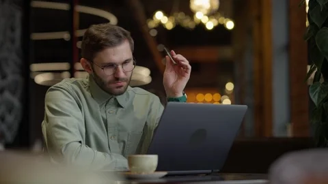 A Focused Young Man Engaged in Thoughtful Work on His Laptop While Sipping Stock Footage 344799934