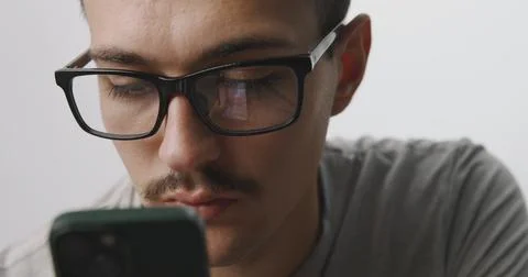 Focused young man with glasses looking down at his smartphone screen on a w.. Stock Photos