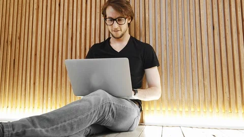 A focused young man in glasses is sitting on the floor and typing on a laptop. Video stock 111719785